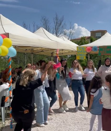 Merkezin bahçesinde düzenlenen bahar şenliğinde çocuklar, veliler ve öğretmenler birlikte halay çekiyor; arkada 'Sevgi varsa engel yok' yazılı pano.